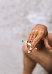 An adult elderly male worker smokes, holding a cigarette in his hands during a smoke break after...