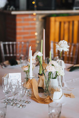 Empty tableware set, candles, tablecloth, flowers, decorated table with glass crystal stand in restaurant indoor. Photography, design concept for banquet.