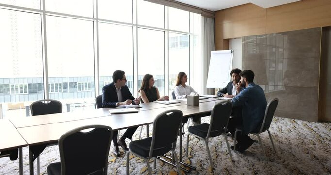 Positive motivated diverse business team talking at large table, brainstorming on creative ideas for project, discussing work tasks, teamwork, cooperation at meeting, smiling, laughing