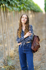 A Stylish Young Woman Dressed in Denim Stands Among the Beautiful Lush Rows of a Vineyard