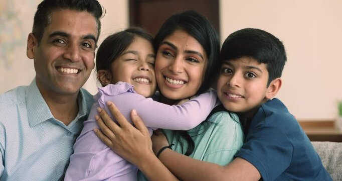 Happy young Indian parents cuddling little daughter and son with love, tenderness, affection, care, hugging sibling kids, looking at camera for portrait, smiling, laughing, enjoying family leisure - Powered by Adobe