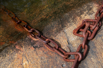 Detail of an old rusty metal chain anchored to a concrete block