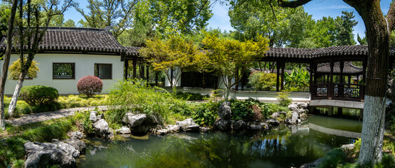 Fototapeta premium A traditional Chinese pavilion overlooks a tranquil pond where koi fish swim. A stone path leads through the garden, with lush greenery, rock formations, and gazebo.Moon Lake Park.Ningbo China