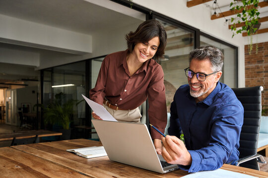 Happy busy executive people working together in office. Female manager showing financial results to colleague at work. Two professional team business man and woman using laptop at corporate meeting.
