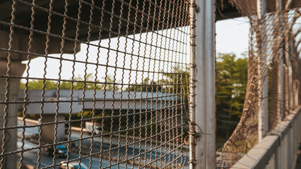 Focused shot of a wire mesh fence framing an elevated highway, conveying urban infrastructure