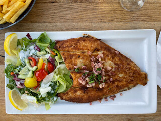 Fried North Sea plaice fish fillet with bacon and fresh green salad on a plate directly above view
