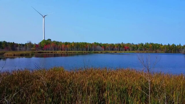 Une &eacute;olienne &agrave; l'arr&ecirc;t sous un ciel bleu voisine un petit lac peu profond ceintur&eacute; d'une for&ecirc;t multicolore au couleurs de l'automne et de bande de roseaux et d'arbres morts. ( Qu&eacute;bec, Canada. )