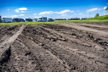 Selective focus on mud and torn up grass in the foreground of a dirt parking lot