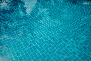 A serene and tranquil swimming pool with a mosaic tiled floor, capturing the reflection of palm trees and a bright sky. 