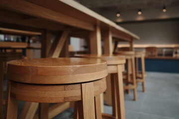 A close-up shot of wooden bar stools arranged around a long wooden table in a modern, minimalist...