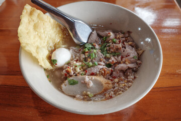 A close-up of a bowl of traditional Thai noodle soup, featuring tender slices of pork, a fish ball, and a crispy wonton on the side.