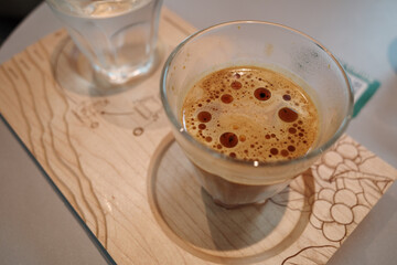 A close-up shot of a freshly brewed espresso served in a clear glass on a decorative wooden tray.