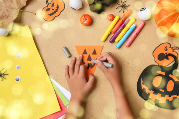 Hands of child making decorations for Halloween celebration on beige background