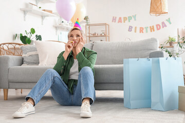 Mature woman in birthday hat with party blower at home
