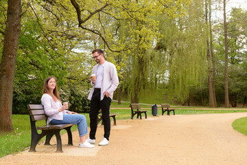 Beautiful loving couple sitting on bench and drinking coffee in park