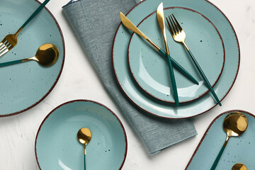 Table setting with clean plates, golden cutlery and napkin on white background