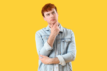 Thoughtful young redhead man on yellow background