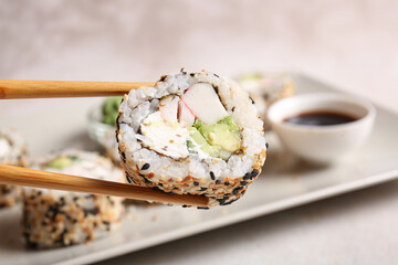 Chopsticks with tasty sushi roll, closeup view