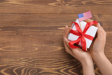 Woman holding gift box with USA flag on brown wooden background. American Independence Day
