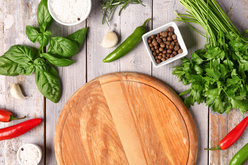 Composition with cutting board, fresh herbs and spices on light wooden background