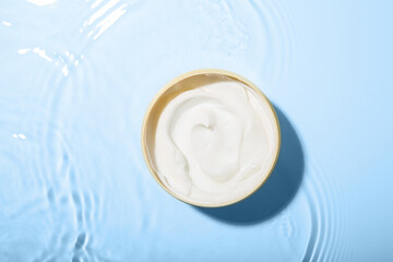 Cosmetic product. Jar with cream in water on light background, top view