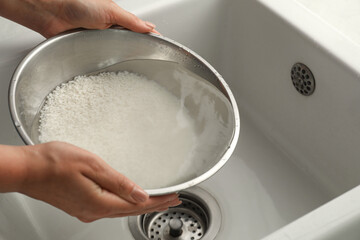 Woman rinsing rice in bowl above sink, closeup
