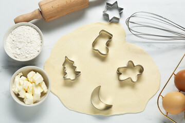 Flat lay composition with raw dough, cookie cutters and ingredients on white marble table