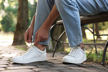 Man tying shoelace of white sneaker outdoors, closeup