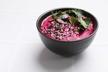 Tasty beetroot hummus, parsley and sesame in bowl on white table, closeup. Space for text