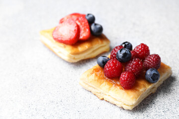 Tasty puff pastries with berries on light grey table, closeup. Space for text