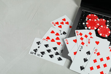 Online poker. Playing cards, chips and laptop on light grey table, space for text