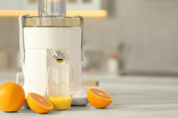 Modern juicer, oranges and glass on white marble table in kitchen, space for text