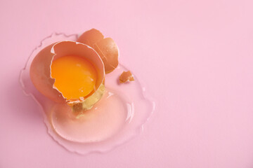 Broken raw egg with shell on pink background, closeup. Space for text