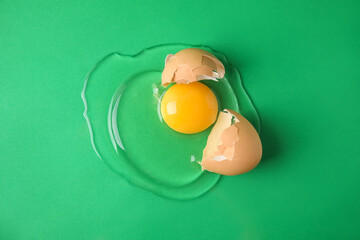 Broken raw egg with shell on green background, top view