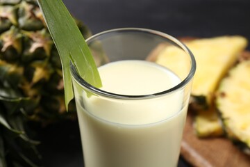 Tasty pineapple smoothie in glass and fruit on black table, closeup