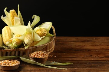 Many fresh ripe corncobs with green husks and kernels on wooden table. Space for text