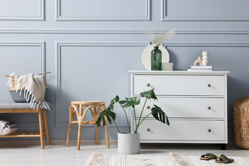 Stylish interior with stool and chest of drawers near light grey wall