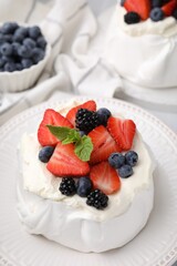 Pavlova cake (meringue dessert) with whipped cream, fresh berries and mint on table, closeup