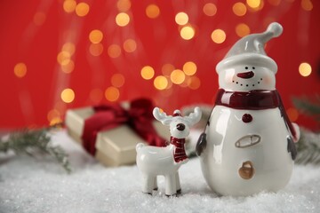 Cute decorative snowman and deer on artificial snow, closeup. Space for text