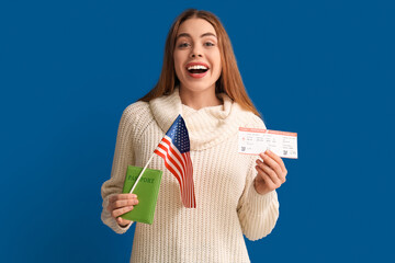 Beautiful young happy woman with USA flag, passport and ticket on blue background