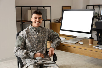 Young male soldier sitting at table with blank computer screen in headquarters