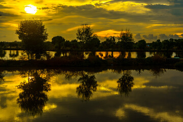 A breathtaking sunset casts golden hues over a tranquil pond near Mengare, Gresik, Indonesia