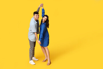 Fototapeta premium Happy young couple dancing on yellow background