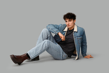 Handsome young man in stylish clothes sitting against grey background