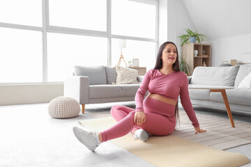 Sporty pregnant woman sitting on fitness mat at home