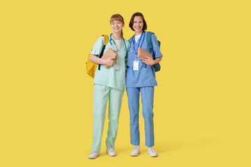 Female medical interns with books on yellow background