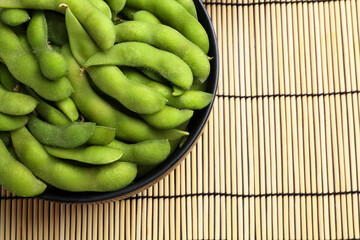 Raw green edamame pods on wicker mat, top view. Space for text