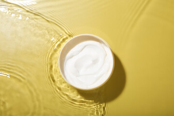 Jar with cream in water on yellow background, top view. Cosmetic product