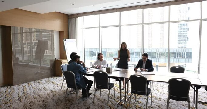 Confident business leader woman speaking to team and boss at meeting, standing at large table, offering ideas for project management, brainstorming, presenting strategy, Full length wide view