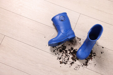 Rubber boots with mud on wooden floor, top view. Space for text